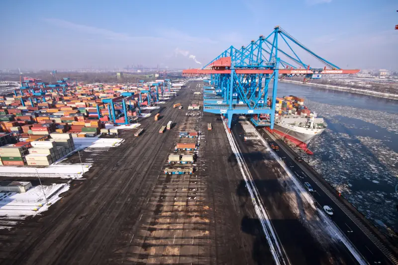 Blick von einer Containerbrücke über ein Containerterminal im Winter, mit Blocklager, Transportfahrzeugen und Eis auf der Elbe.