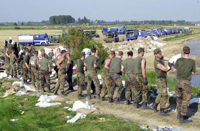 Soldaten reichen am Elbdeich Sandsäcke in einer langen Kette weiter, dahinter Fahrzeuge des THW.