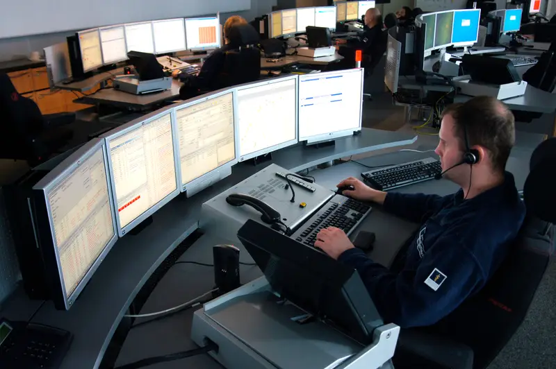 Ein Disponent mit Headset arbeitet in einer Rettungsleitstelle an einem Pult mit fünf Bildschirmen.