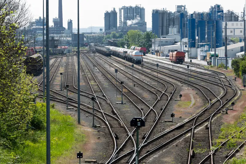Gleisfeld eines Güterbahnhofs mit Kesselwagen, dahinter die Anlagen eines Chemieparks.