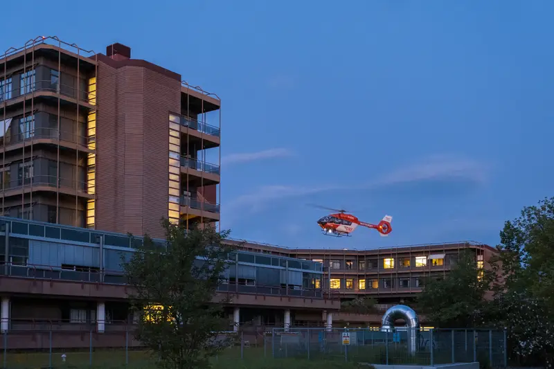 Ein Rettungshubschrauber startet in der Abenddämmerung vom Gelände einer Klinik.
