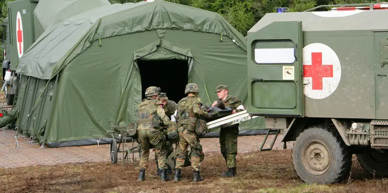 Sanitätssoldaten tragen eine Trage vom Krankenkraftwagen in das Zelt einer Rettungsstation.