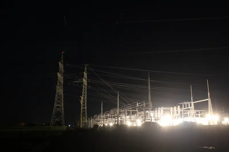 Ein hell beleuchtetes Umspannwerk mit Hochspannungsmasten in der Nacht.